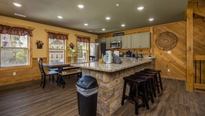 A kitchen with a stone island, wooden cabinets, and a view of the outside. - Pirates Peak (Gatlinburg)