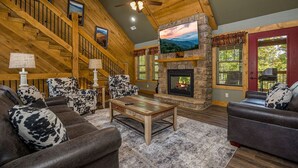 A spacious living room with a fireplace, wooden staircase, and comfortable seating. - Pirates Peak (Gatlinburg)