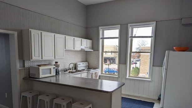 Une cuisine moderne dotée d’un îlot central, de meubles blancs et offrant une vue sur l’extérieur grâce à de grandes fenêtres.