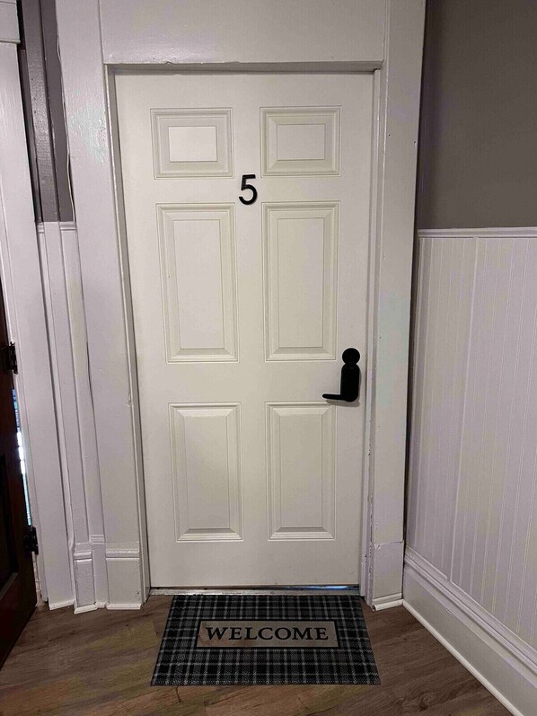 A white door with the number 5, a black doorbell, and a welcome mat.