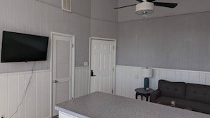 Une chambre dotée d’une kitchenette, d’un ventilateur de plafond, d’un téléviseur à écran plat, d’un canapé et d’une petite table avec une lampe.