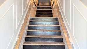 Un escalier avec des marches en bois et des murs blancs, menant à une porte sombre située en haut.