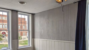 Une chambre à coucher avec un lit, un ventilateur de plafond et une fenêtre donnant sur les bâtiments environnants.