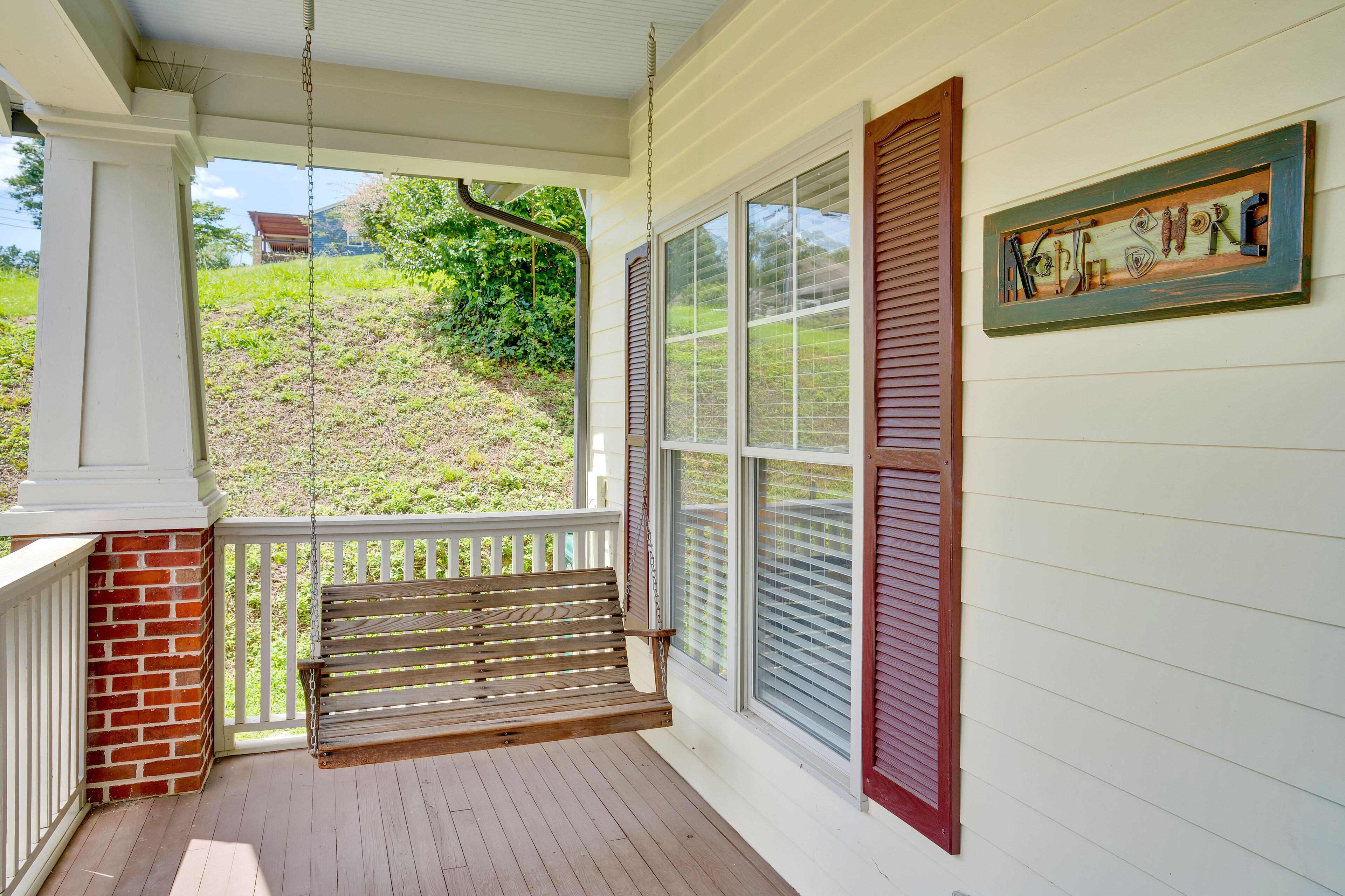 A porch with a wooden swing, white railings, and a view of a green landscape.