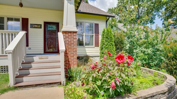 A house with a front porch, steps, a brick column, and a garden with flowers.