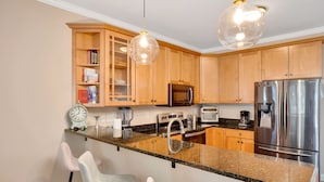 A modern kitchen with wooden cabinets, granite countertops, stainless steel appliances, and pendant lighting.