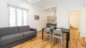 A modern living room with a sofa, dining table, chairs, and a kitchen area with cabinets and a countertop.