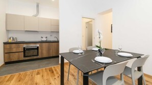 A modern kitchen with wooden cabinets, a built-in oven, and a dining area with a black table and grey chairs.