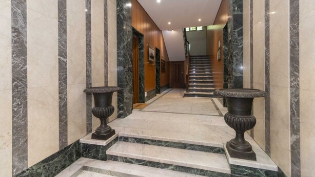 A marble-floored hallway with a staircase, flanked by columns and two large urns.