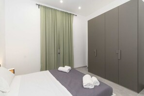 A bedroom with a bed, green curtains, a wardrobe, and two rolled towels on the bed.