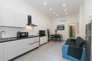 A modern kitchen with white cabinets, a black microwave, and a stove. There is a dining area with a table and chairs, and a sofa in the living room. - GuestHost - Elegant 58m2 apartment that can accommodate up to 4 people located on the mezzanine floor of an elegant building. The property is located in the Cit Turin district a few steps from the M1 Bernini metro which connects the two stations, Porta N (Torino)