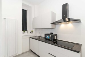 A modern kitchen with white cabinetry, a black microwave, and a stainless steel range hood.