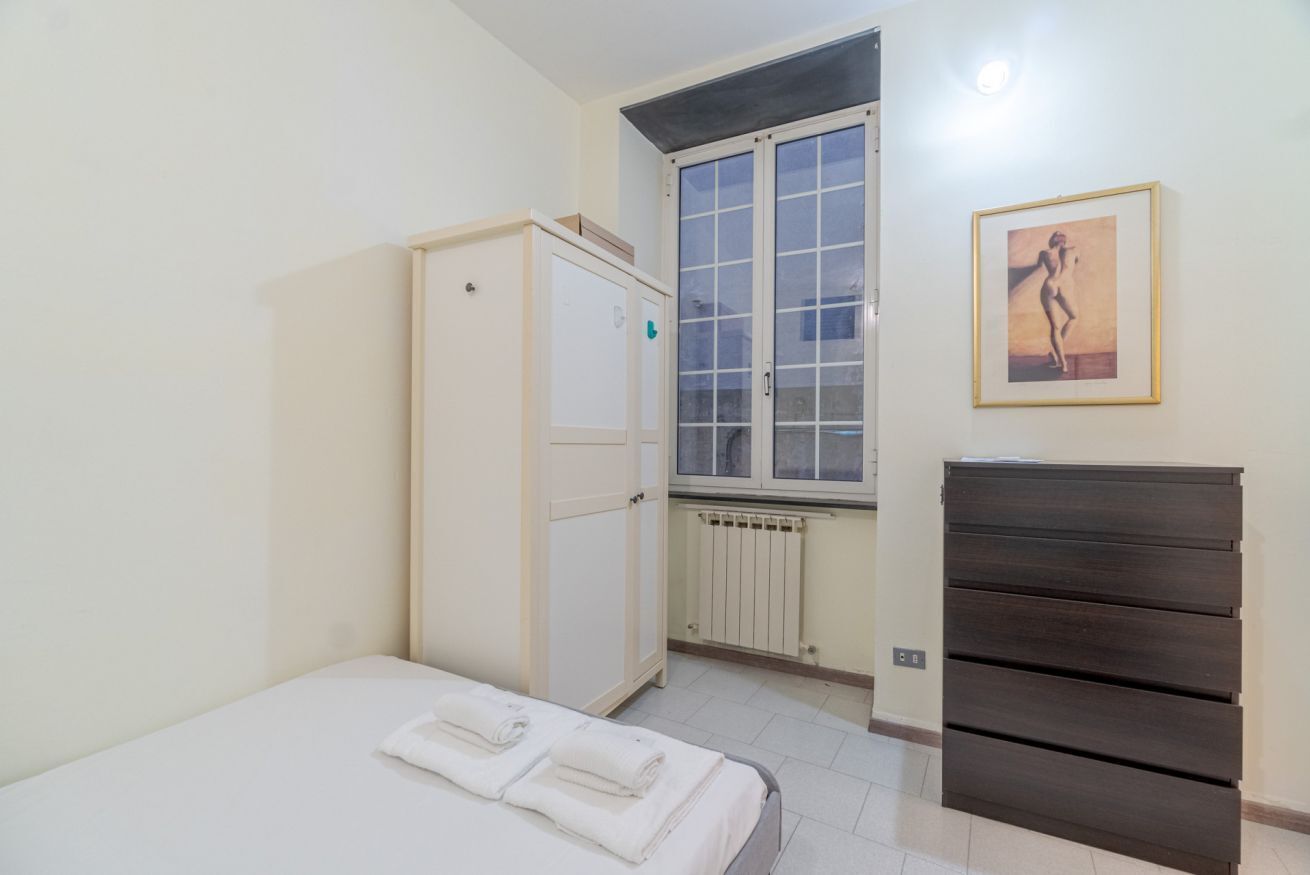 A bedroom with a bed, a wardrobe, a radiator, and a window.