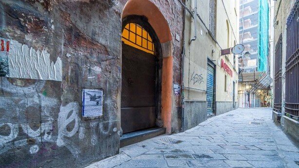 A narrow alleyway with a closed arched doorway, a wall with graffiti, and a sign for 'MUSEETTI.' - GuestHost - Cozy apartment of 50 sqm, able to accommodate up to 4 people, located on the first floor of a building without elevator. The location is great! We are about 300 meters from the Cathedral of San Lorenzo, 200 meters from Palazzo Ducale , 600 fr (Genova)