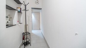 A narrow hallway with white walls, a coat rack, a shelf with toiletries, and a door at the end. - GuestHost - Cozy apartment of 50 sqm, able to accommodate up to 4 people, located on the first floor of a building without elevator. The location is great! We are about 300 meters from the Cathedral of San Lorenzo, 200 meters from Palazzo Ducale , 600 fr (Genova)