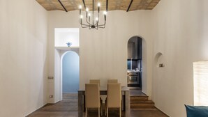 Un comedor amplio con una mesa y sillas, una araña y vista a la cocina a través de un arco.