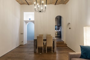 A spacious dining area with a table and chairs, a chandelier, and a view of the kitchen through an archway.