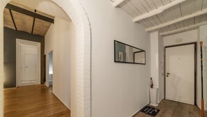 Un pasillo con paredes de ladrillo blanco, suelo de madera, un espejo de marco negro y una puerta blanca.