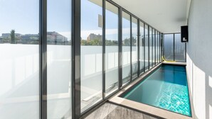 A modern indoor swimming pool with large glass windows offering a view of the cityscape.