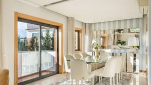 A modern dining area with a glass table and white chairs, a balcony with a view, and striped wallpaper.
