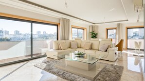 A modern living room with a glass coffee table, a beige sofa, and a city view through large windows.