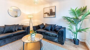 A modern living room with a sofa set, a round coffee table, a floor lamp, a mirror, a painting, and a potted plant. - Lovely 5 Bed House in Egham near Heathrow & Virginia Water (Egham)