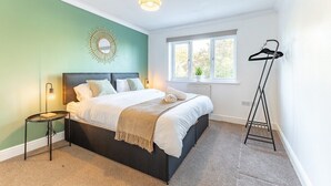 A bedroom with a bed, a bedside table, a hanging light fixture, a window with a view, and a radiator. - Lovely 5 Bed House in Egham near Heathrow & Virginia Water (Egham)
