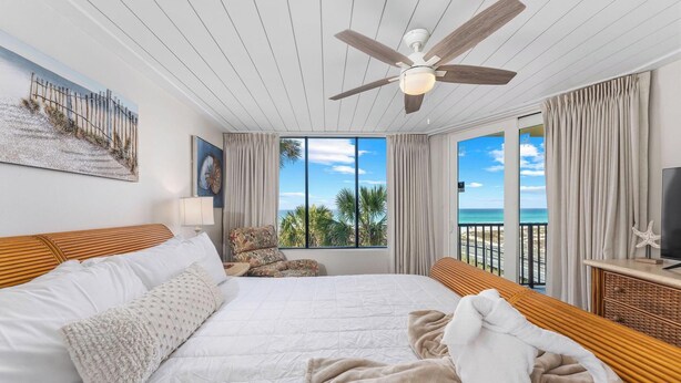 Une chambre à coucher avec un lit, un ventilateur de plafond, une télévision et une vue sur l’océan.