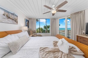 A bedroom with a bed, a ceiling fan, a TV, and a view of the ocean.