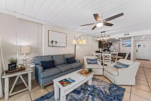 A living room with a sofa, armchairs, a coffee table, a ceiling fan, and a dining area with a table and chairs.