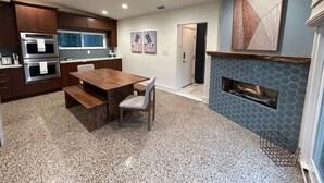 A modern kitchen with built-in appliances, a dining area with a wooden table and chairs, and a stone fireplace.