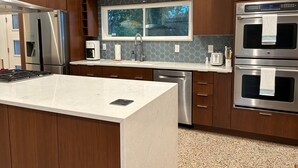 A modern kitchen with stainless steel appliances, a large island, and a window with a view of trees.