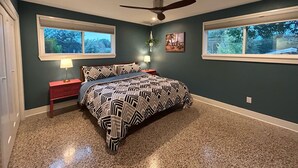 A bedroom with a bed, two bedside tables, a ceiling fan, and two windows.