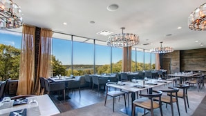 Un restaurante con mesas y sillas, ventanas amplias y candelabros de cristal colgantes.