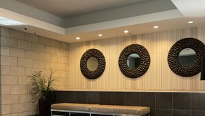 Un hall d’entrée moderne avec un banc, une plante en pot et trois miroirs fixés au mur.