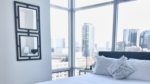 Une chambre d’hôtel moderne avec un grand lit, une vue sur la ville et un miroir encadré au mur.
