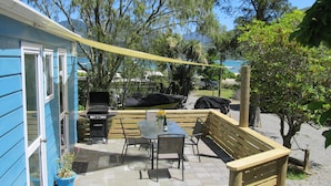 En terrasse med et bord, stole, grill og en blå bygning med vinduer.