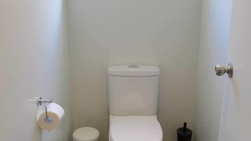 A small, clean bathroom with a toilet, a trash can, and a window above the toilet.