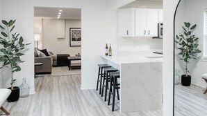 Een moderne keuken met witte kasten, een marmeren aanrechtblad en een bar voorzien van krukken.