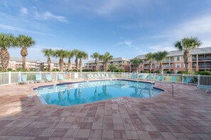A swimming pool with a tiled deck, surrounded by palm trees and a white fence. - Atlantis 205B - Beachers Landing - Renovated (St. Augustine Beach)