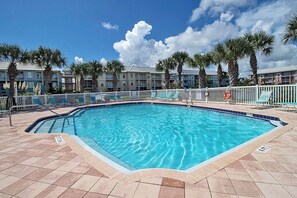 A rectangular swimming pool with a tiled edge, surrounded by a white fence, and palm trees in the background. - Atlantis 205B - Beachers Landing - Renovated (St. Augustine Beach)