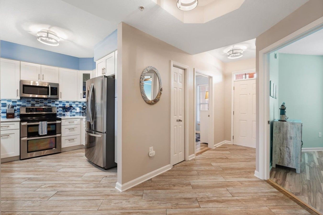 A modern kitchen with stainless steel appliances, a herringbone wood floor, and a hallway leading to bedrooms.