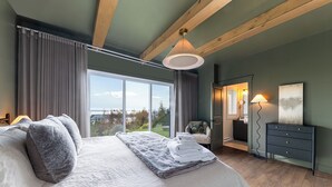 Un dormitorio con una cama grande, una silla, un aparador y vistas al exterior.