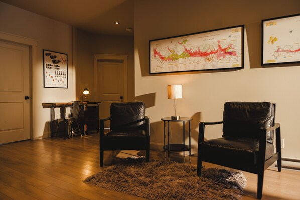 A room with two leather chairs, a small table, a lamp, and a rug. There are framed maps on the wall.