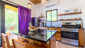 A modern kitchen with a central island, stainless steel appliances, and wooden cabinetry. - La Joya Amatista - Walk to Beach (Nosara)