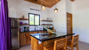 A modern kitchen with wooden cabinets, a black countertop, and a central island with chairs. - La Joya Amatista - Walk to Beach (Nosara)