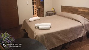 Ein ordentlich bezogenes Bett mit zwei weißen Handtüchern, einem hölzernen Kopfteil, einem kleinen Nachttisch mit Lampe und einem eingebauten Kleiderschrank mit mehreren Regalen.