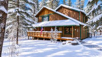 Una cabaña de madera con porche, rodeada de árboles cubiertos de nieve.