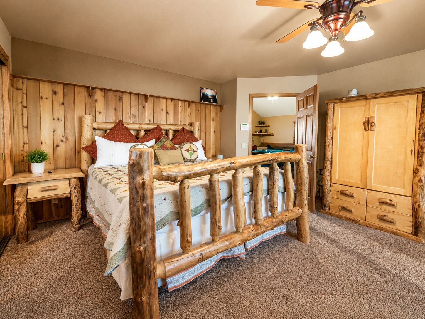 A wooden-framed bed with a headboard, a nightstand with a plant, and a wardrobe with a mirror.