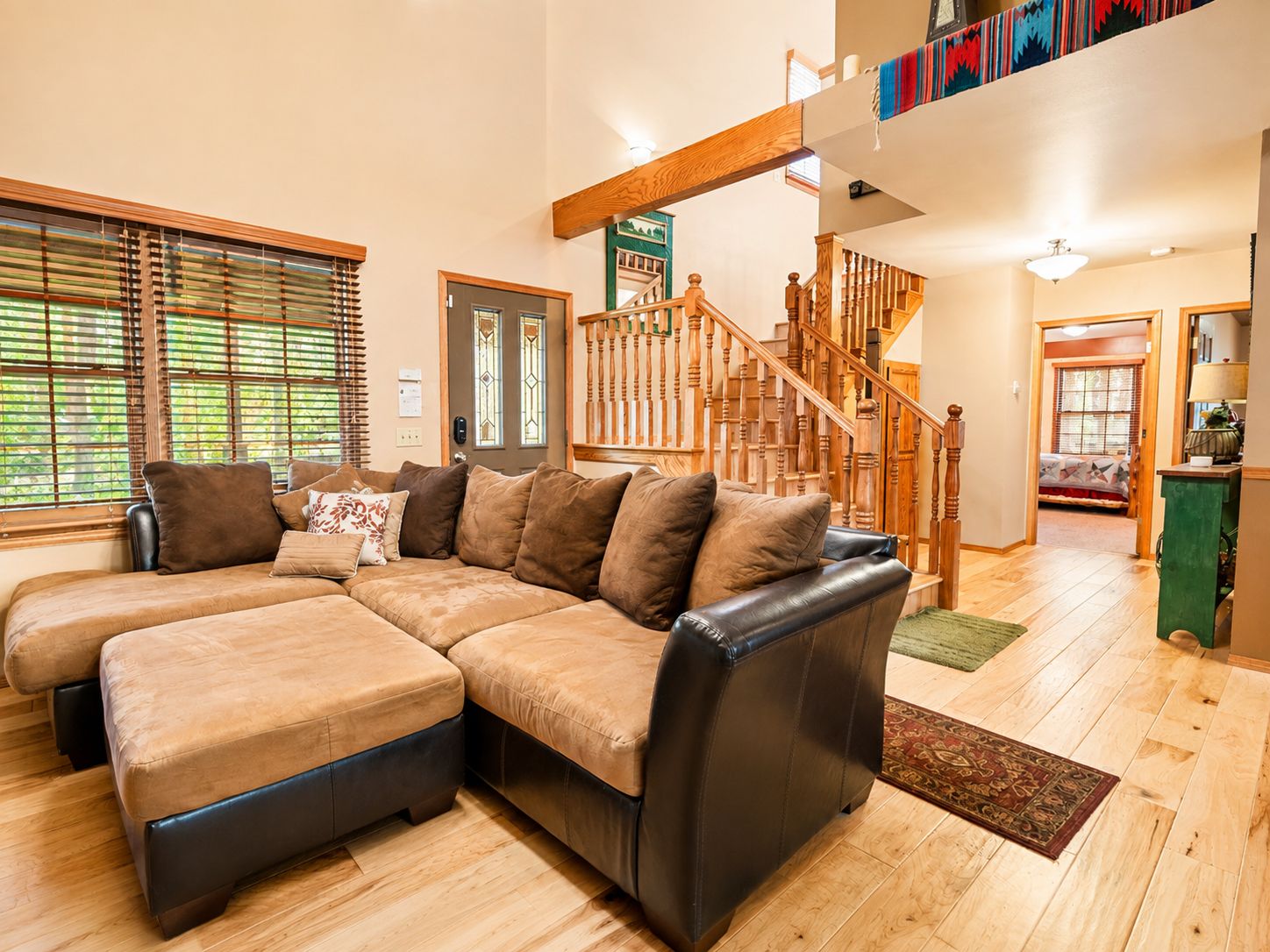 Una sala moderna con un sofá modular, suelo de madera, una escalera y vistas al piso superior.
